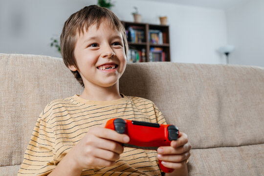 Smiling child playing video game with joystick at home on sofa