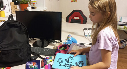 Young girl unpacking school supplies at home desk with backpack