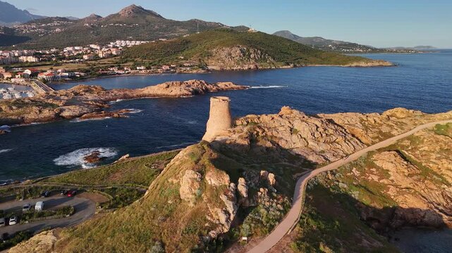 Dynamic aerial drone boomerang shot orbiting the historic Genoese Tower on the rugged Pietra Peninsula, L'&Icirc;le-Rousse, Corsica, France.