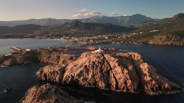 Expansive Aerial Drone Pan Out Over Turquoise Mediterranean Sea Revealing Pietra Peninsula and L'&Icirc;le-Rousse Coastal Town, Corsica, France.