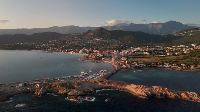Expansive Aerial Wide Shot Showcasing the Beautiful Coastal Setting of L'&Icirc;le-Rousse, Corsica, with Blue Mediterranean Sea and Lush Mountains.