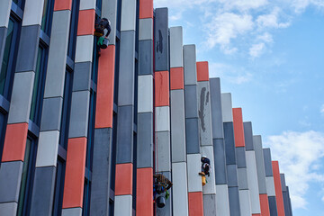 Window washers cleaning windows on modern office building facade. High rise window cleaners using rope access. Industrial alpinists washing exterior of skyscraper. Dangerous risky work at height