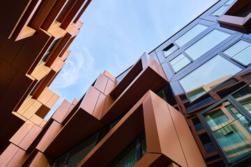 Low angle view of a modern building with angular metal panels and large glass windows. Concept of contemporary architecture, geometric design and urban construction.