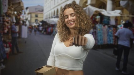 Young woman pointing hand forward holding a takeout box on a busy street; friendly invitation welcome joy.