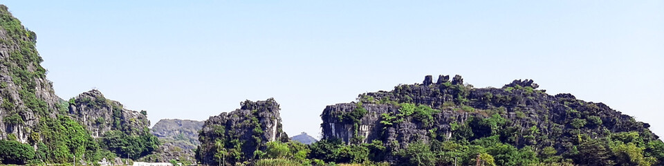 Fototapeta premium Dramatic Limestone Karst Mountains Covered In Lush Green Vegetation Under A Clear Blue Sky