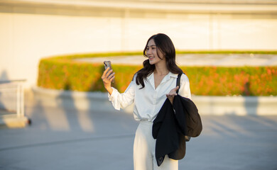 Confident Asian businesswoman smiling in a modern corporate setting, attractive professional lady standing outdoors, showcasing success, beauty, career ambition, and cheerful lifestyle.