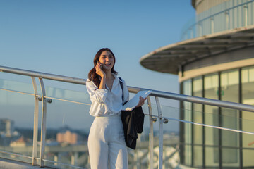 Confident Asian businesswoman smiling in a modern corporate setting, attractive professional lady standing outdoors, showcasing success, beauty, career ambition, and cheerful lifestyle.