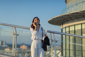 Confident Asian businesswoman smiling in a modern corporate setting, attractive professional lady standing outdoors, showcasing success, beauty, career ambition, and cheerful lifestyle.
