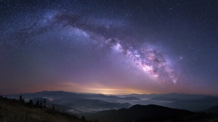 Fototapeta premium Milky way galaxy arching over mountain landscape with distant glow