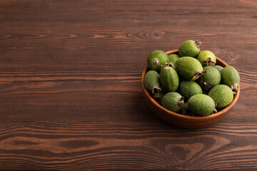 Ripe Feijoa in wooden bowl on brown wooden, side view, copy space