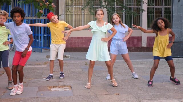 Confident positive preteen boys and girls dancing modern choreography on city street on sunny summer day