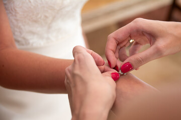 The maid of honor with red nails helping fasten the bracelet on the bride’s wrist. A moment from...