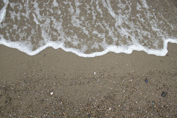 White foam touches wet sand with tiny pebbles and grains. Natural coastal texture, serene mood, perfect minimalist background with room for text.