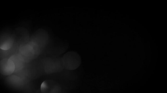 Soft, out-of-focus white bokeh lights drift and fade on a black background. A seamless loop overlay for creating a cinematic, dreamy, or festive mood