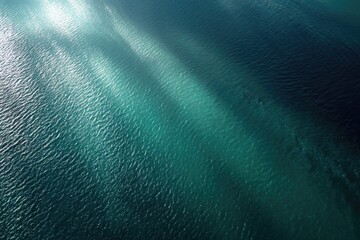 Aerial view of shimmering aquamarine ocean with sun rays creating long, diagonal streaks