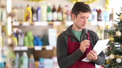  Adult man seller conducting inventory with checklist in household chemicals store decorated for christmas