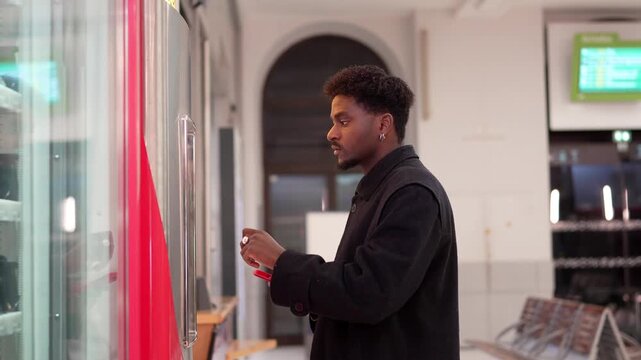 Young african american man using vending machine at train station