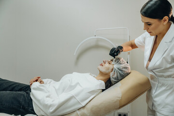 Dermatology conception. Female cosmetologist performing a facial skincare procedure using a cosmetic device in a beauty clinic