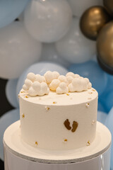 Trendy baptism cake with figure clouds and golden decor baby footprint. Celebration baptism concept. Delicious reception at birthday baby party. Cake in background photo zone. Closeup. Side view.