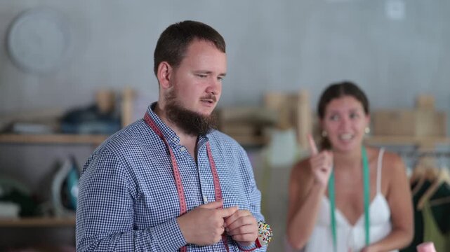 Upset male dressmaker being scolded by angry woman standing behind in sewing workshop. High quality 4k footage