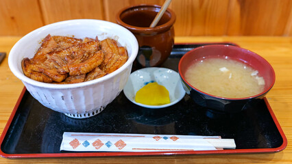 A traditional Japanese set meal featuring a bowl of grilled pork on rice (butadon), miso soup, pickled radish, and a small teacup