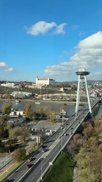View of Bratislava city center with the historic castle on the hill and cars driving on the snp bridge across the danube river under a blue sky. 