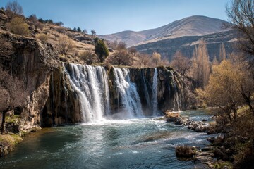 Obraz premium A majestic, wide waterfall cascades powerfully into a pristine river, creating a captivating display of nature's force and beauty. The multiple tiers of the falls tumble over rugged, textured rock for