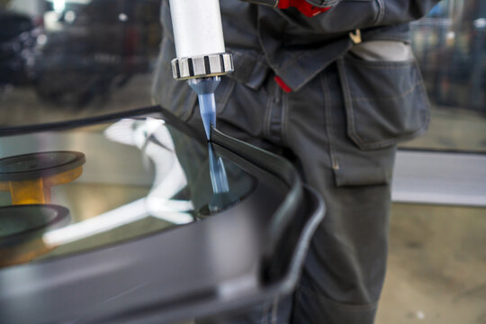Automobile special workers replacing windshield of a car in auto service station garage. The process of car repair. Applying glass adhesive sealant to a new windshield before installation. Accident. 