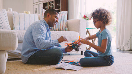 Grandfather And Granddaughter Sitting On Floor in Lounge At Home Building Construction Kit Together
