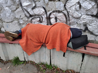Homeless destitute man in black hat with red cover sleep on a bench
