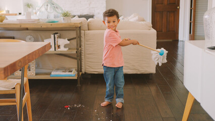 Portrait Of Young Boy Helping With Chores Using Floor Mop At Home