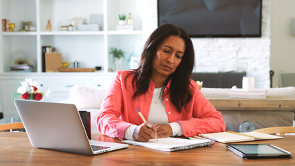 Mature Woman Sitting At Table At Home Checking Finances On Laptop