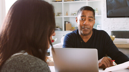 Mature Couple Sitting At Table At Home Checking Finances On Laptop Together