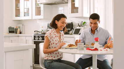 Couple In Kitchen Sitting At Table Eating Meal Together