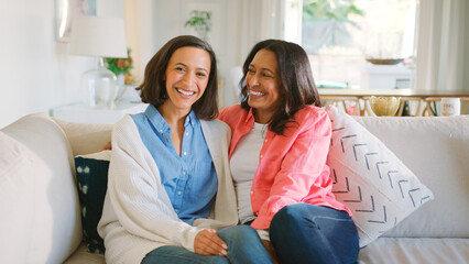 Portrait Of Smiling Mature Mother And Adult Daughter Sitting On Sofa At Home Together