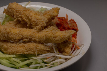 Crunchy breaded chicken strips atop crisp cucumber and bean sprout salad, golden coating, tangy slaw and sliced tomato, crunchy bite contrast with cool greens