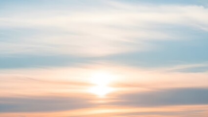 Fototapeta premium Soft pastel sunlight spreads through delicate layered clouds, creating a calm, dreamy sky in warm peach and cool blue tones at the horizon.