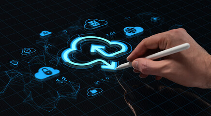 Hand using stylus to interact with glowing cloud upload icon on futuristic digital interface screen with technology symbols on dark grid background.