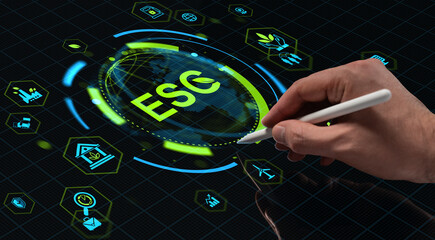 Hand using pen to interact with futuristic ESG user interface concept on digital screen with technology and business icons on grid background.