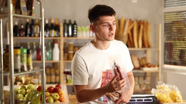 Thoughtful young male customer is deciding on dried sausage and meat in a small market