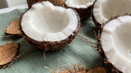 Fresh coconut halves with white juicy pulp on green fabric cloth surrounded by broken brown shell pieces in natural light