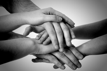 Group of people stacking their hands together, closeup. Black-and-white toning