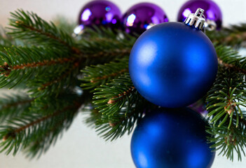 Blue Christmas bauble and fir branch on a reflective surface. Festive holiday decorations with purple ornaments in the background. Winter season concept