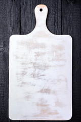 White wooden cutting board on black wooden background. Rustic kitchen utensil