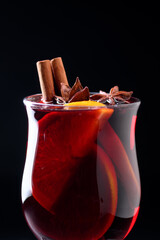 Close up of hot mulled wine in a glass with slice of fresh orange and cinnamon sticks on a black background. Food and drink photography