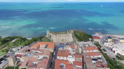 Aerial view of Ortona with azure sea, historic streets and the cliffside Castello Aragonese under a blue sky.