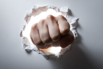 Powerful human fist violently breaks through white paper barrier revealing bright light and opportunity beyond
