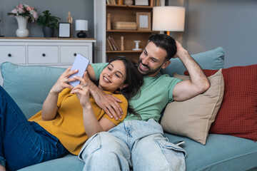 Couple relaxes together, taking a selfie on a smartphone, laughing at messages, sharing photos, scrolling the feed, planning weekend, replying to friends, and saving moments to the gallery today