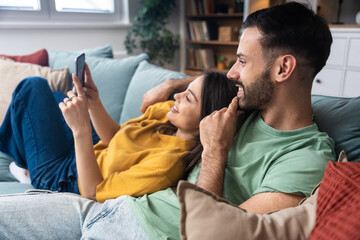 Couple relaxes together, taking a selfie on a smartphone, laughing at messages, sharing photos, scrolling the feed, planning weekend, replying to friends, and saving moments to the gallery today