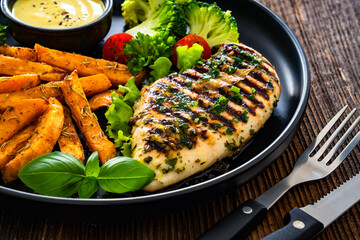 Grilled chicken breast, sweet potato fries with barbecue sauce and boiled broccoli on wooden table
